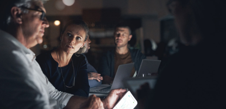 Mature man looking at screen at night with woman questioning