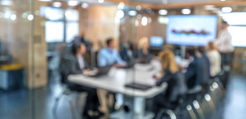 Blurred image of a team around a board table looking at a screen a one end