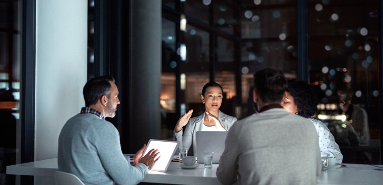 Four workers sitting around a table with laptops having a meeting in the evening