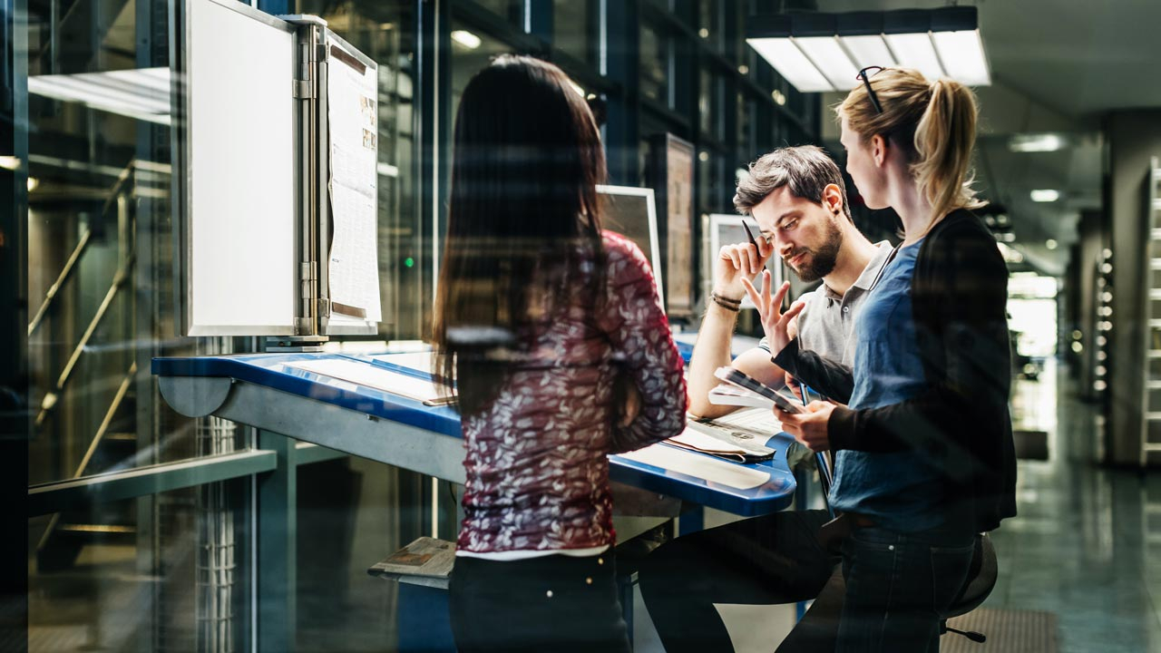 A workteam standing around a high desk talking