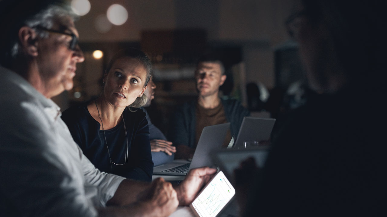 Mature man looking at screen at night with woman questioning