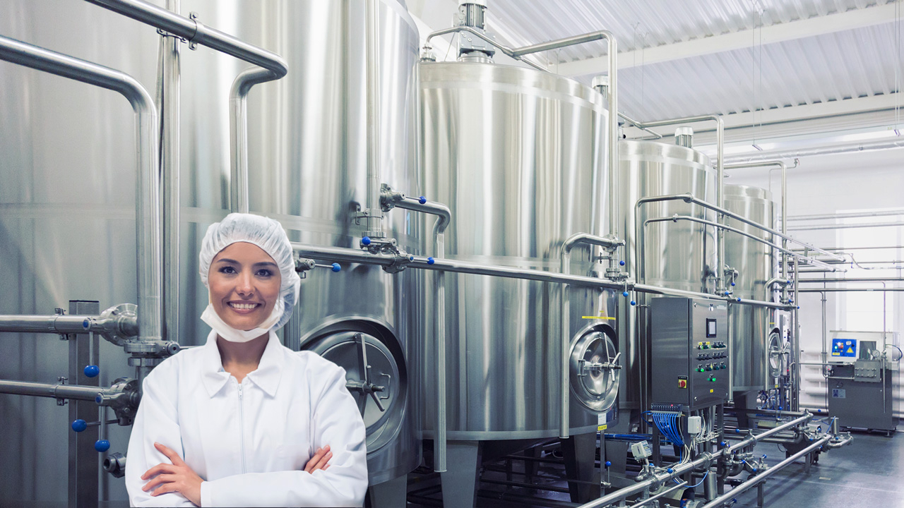 Female worker in full PPE in front of large vats