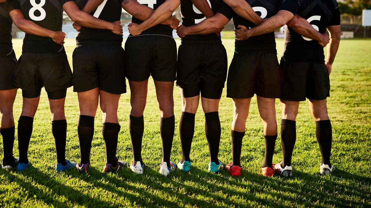 Rugby players in a line with arms round each other facing away from camera