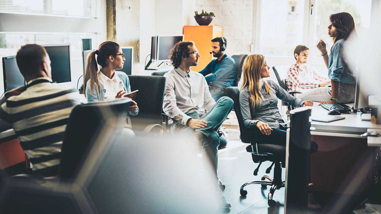 Business team in open plan office listening to co-worker