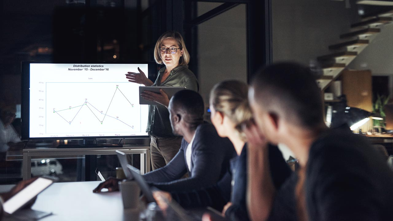 Female leader talking to her team round a table with a whiteboard