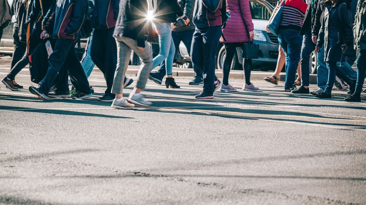People from the waist down walking across a road crossing