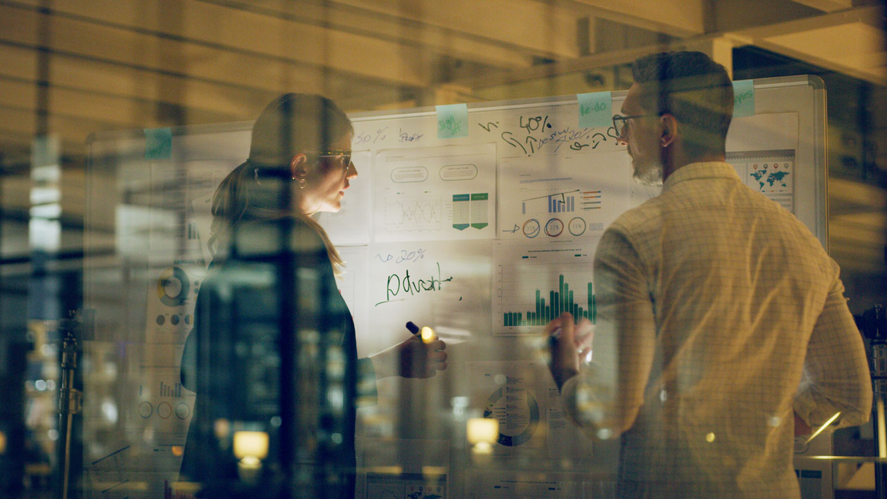 Two people standing looking at a white board in low light