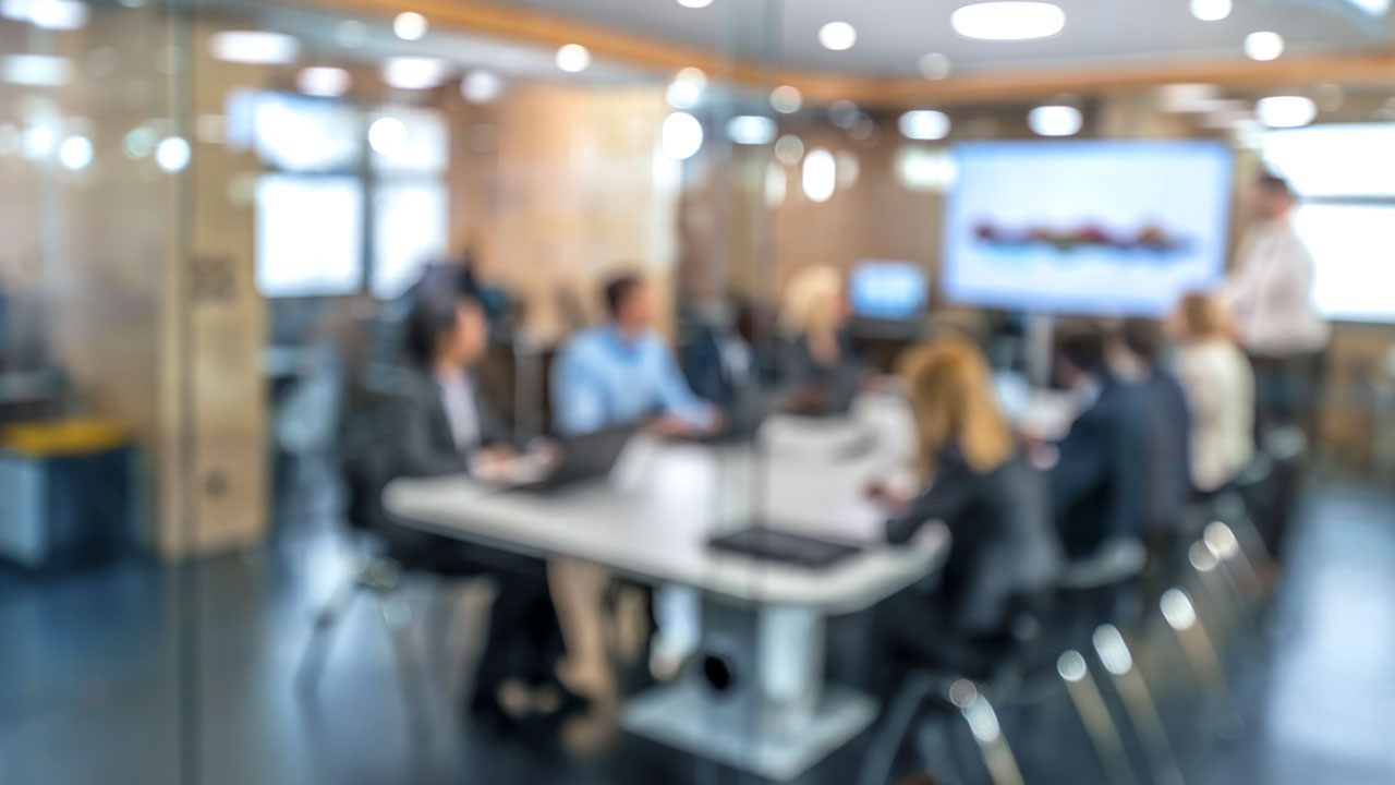 Blurred image of a team around a board table looking at a screen a one end
