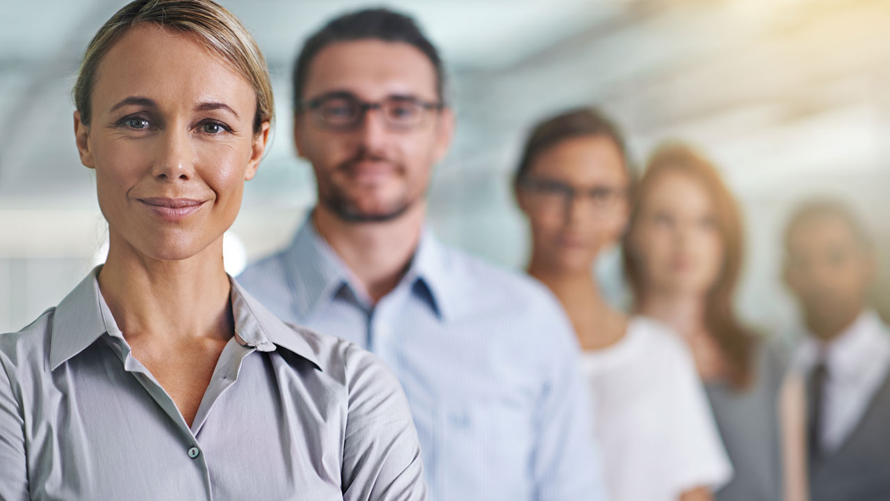 Office workers in a line, first woman in focus, all looking at camera