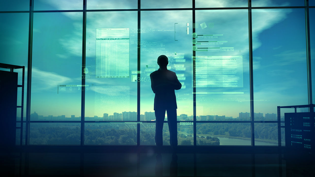 Man standing looking out a window at a sunset over a city 