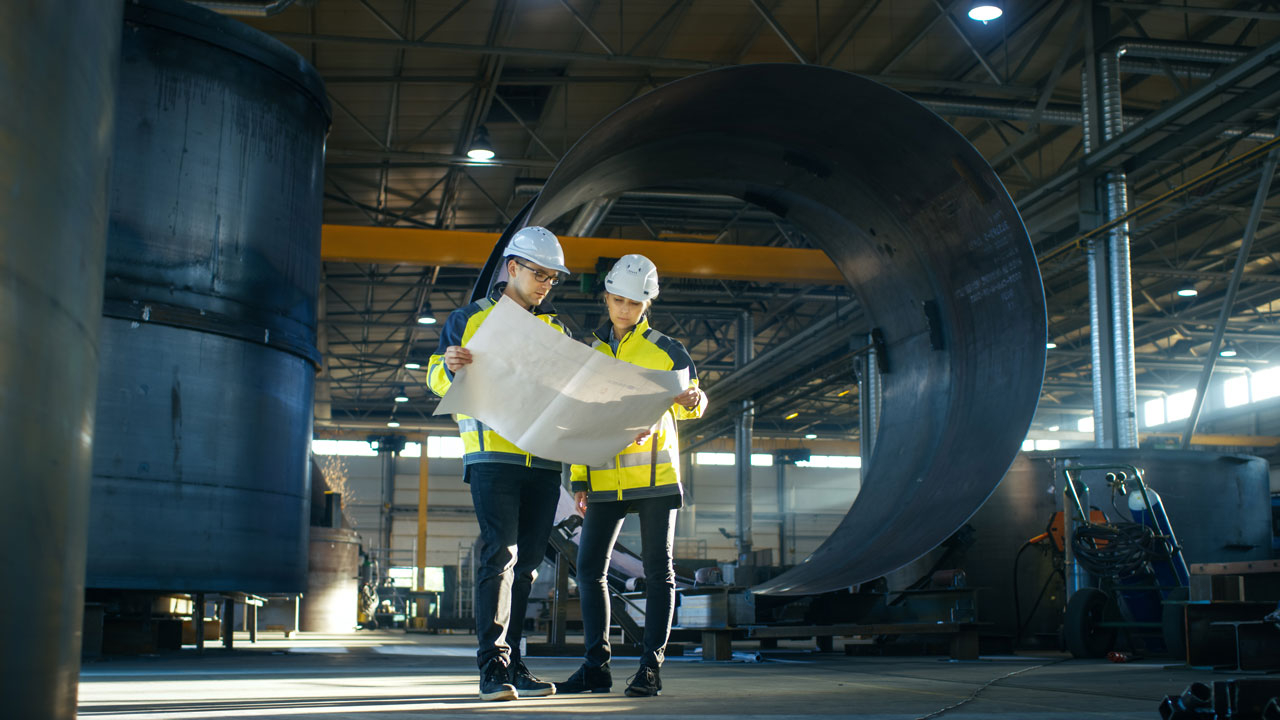 wo workers in high vis jackets and helmets on a worksite looking at a plan
